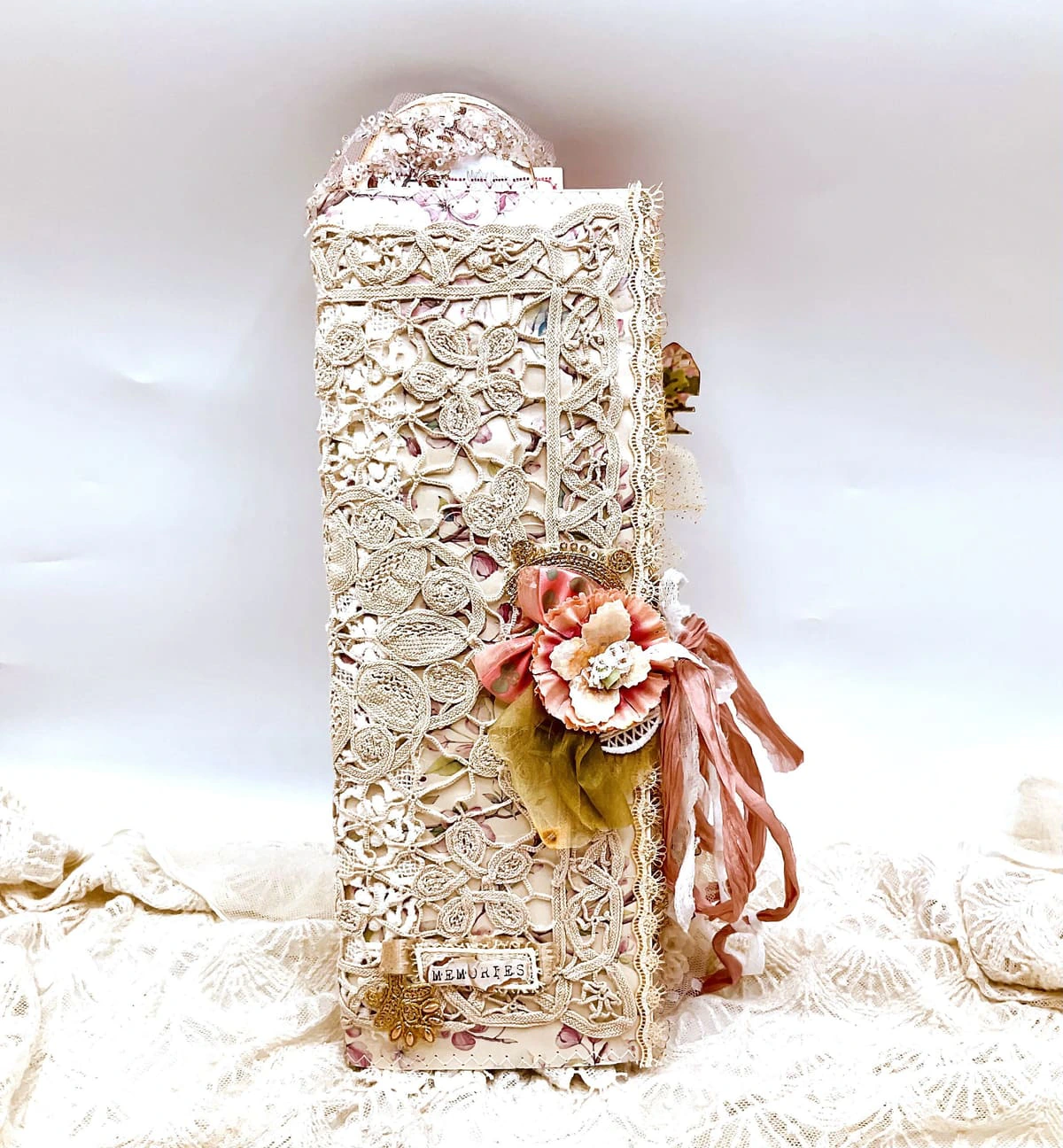 A tall handmade Trinketz journal covered in lace with a silk flower