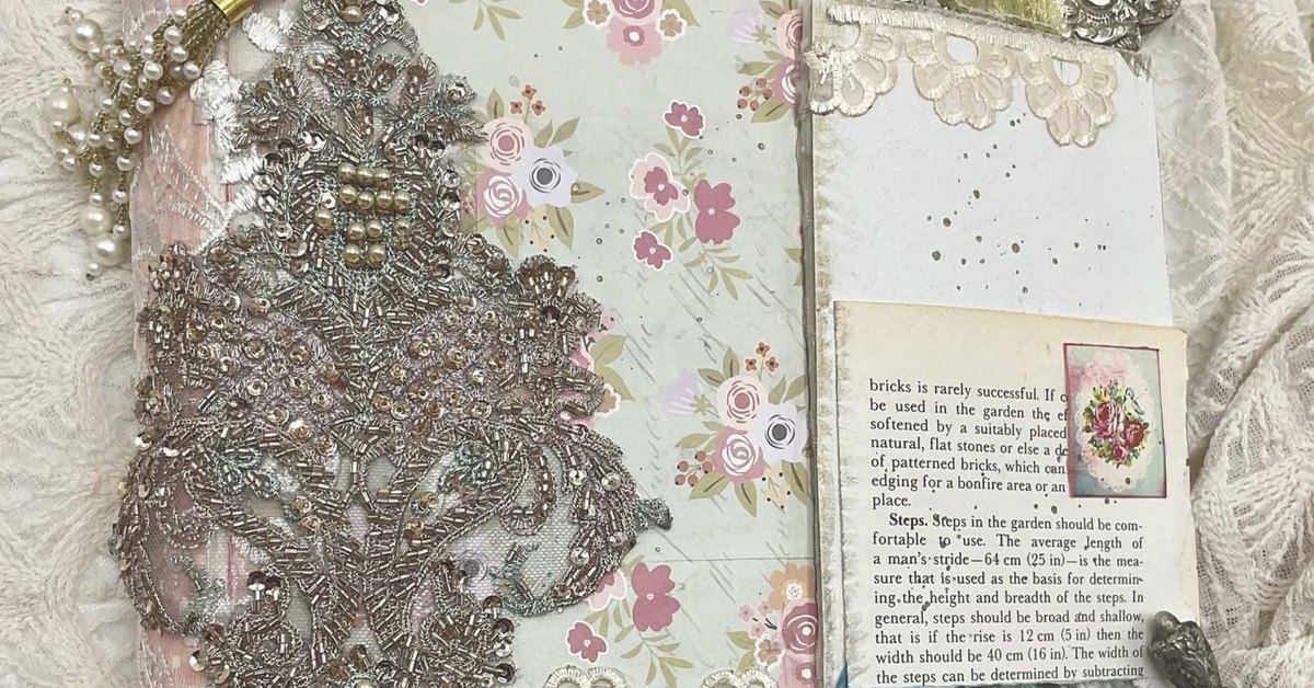 An open handmade journal with a beaded silver appliqué, pearls, lace and floral papers