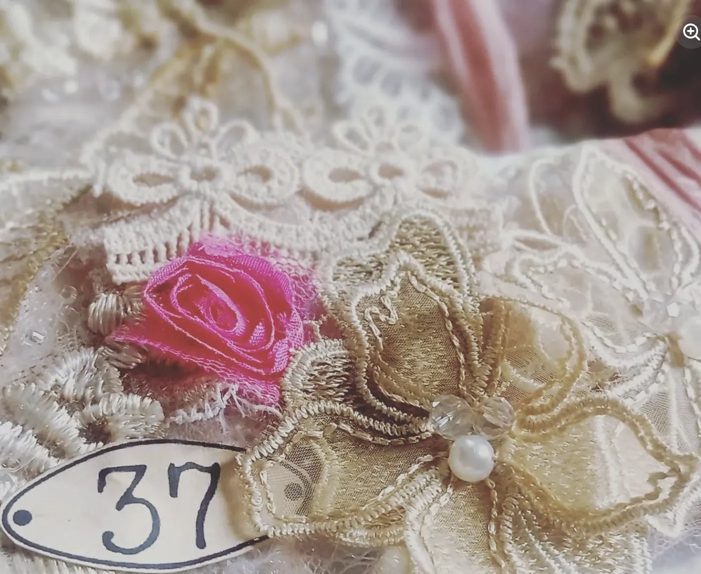 A numbered tag, a pink rose and gold trim on layered lace