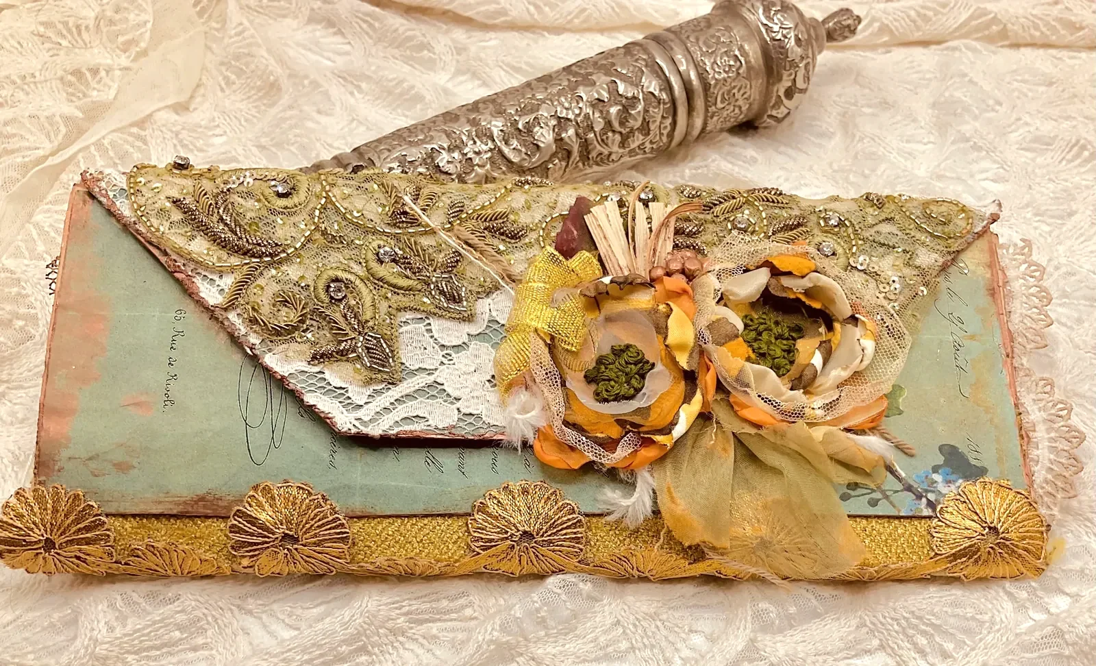 Open artist’s book layered with lace, gold embroidery and handmade flowers